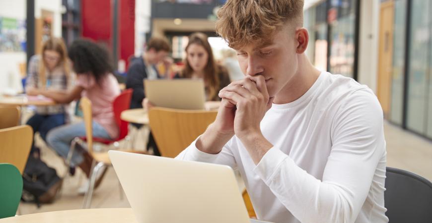 Young man in the library looking at a laptop